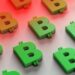 An array of 3D Bitcoin symbols, depicted in green and orange, is arranged on a reflective surface. The top part of the image fades into a red gradient background, creating a visually striking contrast that highlights the emergence of stablecoins. | eCryptoBit