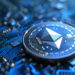 A close-up of a computer motherboard with a large Ethereum (ETH) coin standing vertically. The coin features the Ethereum logo in the center and is surrounded by intricate circuitry, symbolizing its role in powering top Ethereum Dapps. The overall color palette is blue and metallic, emphasizing a high-tech feel. | eCryptoBit